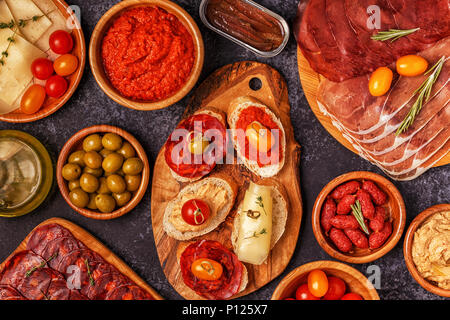 Typical spanish tapas concept. Concept include slices jamon, chorizo, sausage, bowls with olives, tomatoes, anchovies,  mashed chickpeas, cheese. Stock Photo
