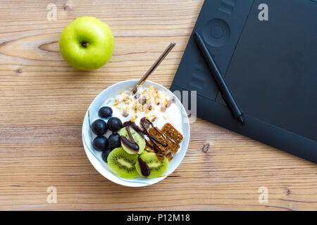 Graphic design and healthy lifestyle concept, top view of cup with raw bars and grape, kiwi fruits inside. Tablet and green apple behind on wooden tab Stock Photo
