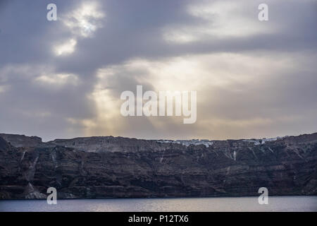 Santorini, Greece: Early morning sunshine breaks through the clouds to shine on white buildings on the rim of the Santorini caldera. Stock Photo