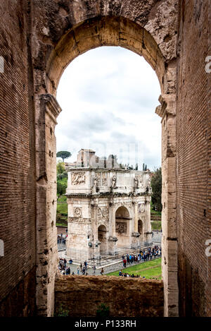 View of The Arch of Constantine from the Colosseum (Colosseo) with Palatine Hill in the background framed by arch of the Colosseum on a cloudy day. Stock Photo