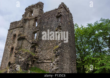 Invergarry, Scotland - June 11, 2012: Tall dark-brown ruined wall with window openings of castle Invergarry, set in green forest under light blue sky. Stock Photo