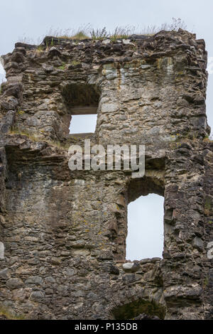 Invergarry, Scotland - June 11, 2012: Closeup of Tall dark-brown ruined wall with window openings of castle Invergarry, under gray sky. Stock Photo