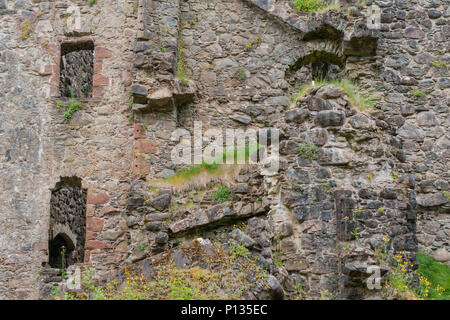 Invergarry, Scotland - June 11, 2012: Tall dark-brown ruined wall with window openings of castle Invergarry. Weeds grow over it. Stock Photo