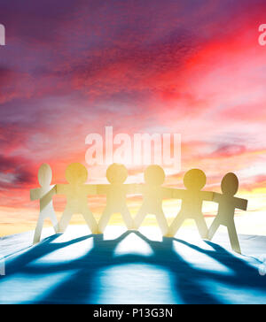 Team of six paper chain people holding hands in front of bright sky Stock Photo