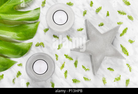 Green leaves, concrete star and candle holders on marble background. Flat lay composition.