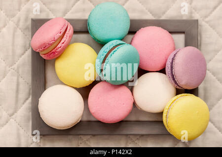 Fresh natural colorful macarons of different tastes in wooden frame on light napkin, top view, unusual abstract sweet art, gourmet gift Stock Photo