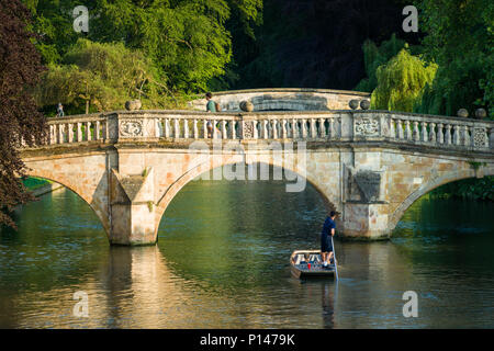 A man steers a punt boat with a couple in towards a stone bridge near Clares college, Cambridge, UK Stock Photo