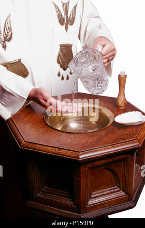 A clergy in a white robe pours water over a baptismal font Stock Photo