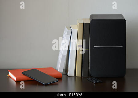 bookshelf speaker with books, smartphone and remote controller on a TV stand Stock Photo