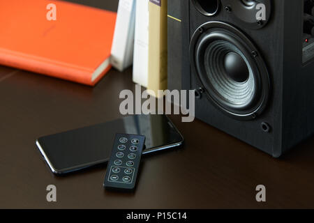 bookshelf speaker with books, smartphone and remote controller on a TV stand Stock Photo