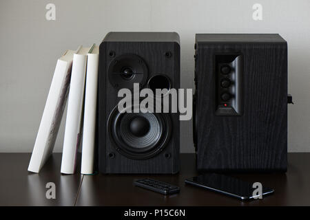 bookshelf speaker with books, smartphone and remote controller on a TV stand Stock Photo