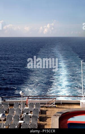 A blue sun lounger at the stern of a cruise ship with the wake in the ...