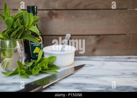 Fresh sprigs of mint leaves in water with a bottle of balsamic vinegar and a dish of sugar ready to make mint sauce Stock Photo