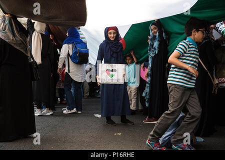 London, UK. 10th June, 2018. A girl stands with a 'Free Palestine' sign underneath a giant Palestinian flag being held up outside the Saudi embassy before hundreds of people take part in the pro-Palestinian Al Quds Day march through central London organised by the Islamic Human Rights Commission. An international event, it began in Iran in 1979. Quds is the Arabic name for Jerusalem. Credit: Mark Kerrison/Alamy Live News Stock Photo