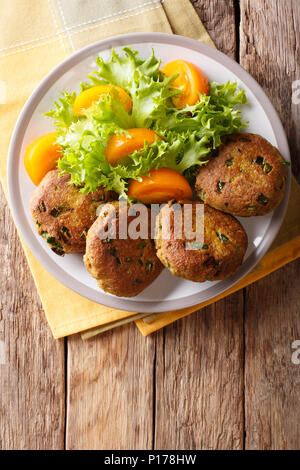 Homemade pancakes made of tuna with spices are served with fresh vegetable salad close-up on a plate on the table. vertical top view from above Stock Photo