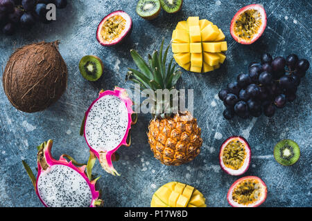 Tropical fruits on stone background, flat lay, table top view. Pitaya, passion fruit, grapes, kiwi, coconut, mango and pineapple Stock Photo