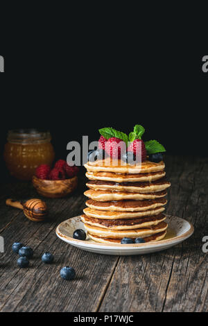 Stack of pancakes topped with fresh berries and honey on rustic wooden table. Homemade pancakes with raspberries and blueberries. Copy space for text Stock Photo