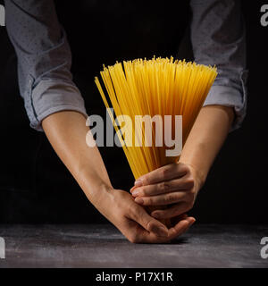 view bunch of raw spaghetti in female hands on black wood vintage table Stock Photo
