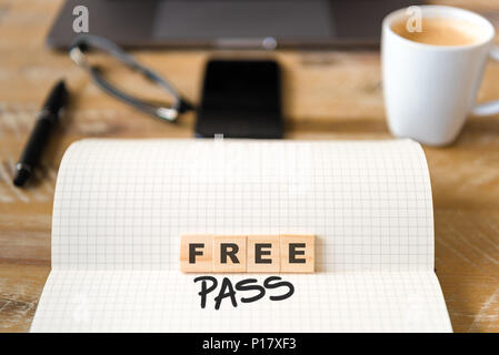 Closeup on notebook over vintage desk surface, front focus on wooden blocks with letters making Free Pass text. Stock Photo