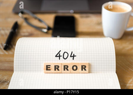 Closeup on notebook over vintage desk surface, front focus on wooden blocks with letters making 404 Error text. Stock Photo
