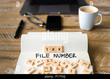 Closeup on notebook over vintage desk surface, front focus on wooden blocks with letters making Tax File Number TFN text. Stock Photo