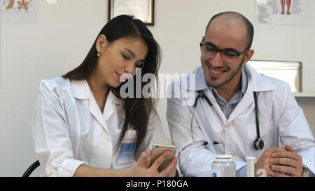 Pretty young nurse showing something funny on her phone to male colleague Stock Photo
