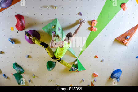 Young man climbing bouldering route, doing splits to reach next handhold. In indoor climbing gym. Stock Photo