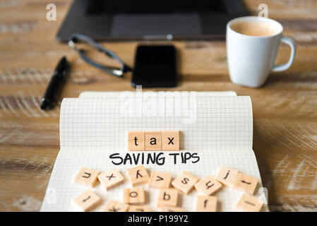 Closeup on notebook over vintage desk surface, front focus on wooden blocks with letters making Tax Saving Tips text. Stock Photo