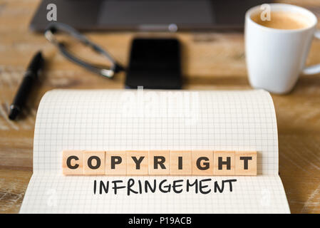 Closeup on notebook over vintage desk surface, front focus on wooden blocks with letters making Copyright Infringement text. Stock Photo