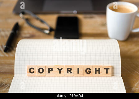 Closeup on notebook over vintage desk surface, front focus on wooden blocks with letters making Copyright text. Stock Photo