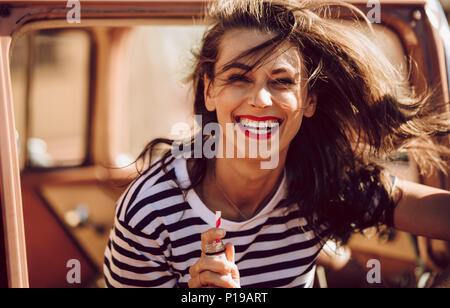 Close up portrait of smiling young woman sitting in a car with beverage bottle. Woman enjoying on a road trip. Stock Photo