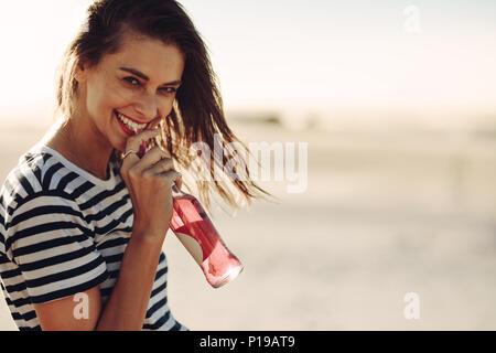 Young smiling woman drinking a soft drink on summer day. Caucasian female enjoying a drink outdoors and looking at camera. Stock Photo