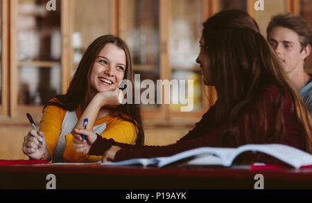 Smiling young woman sitting in the classroom and talking with classmates. university students in classroom during lecture. Stock Photo