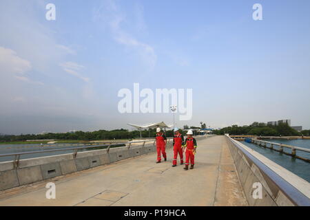Three industrial workers in red working attire walking along marina barrage dam. Singapore. Stock Photo