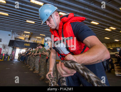 161003-N-TH560-1123 HONG KONG  (Oct. 3, 2016) Seaman Cody Williams, from Woodbridge, Va., and Marines, assigned to 31st Marine Expeditionary Unit, heave a line in the hangar bay of amphibious assault ship USS Bonhomme Richard (LHD 6) during a replenishment at sea (RAS). Bonhomme Richard, flagship of the Bonhomme Richard Expeditionary Strike Group, is operating in the South China Sea in support of security and stability in the Indo-Asia Pacific region. (U.S. Navy photo by Petty Officer 3rd Class Jeanette Mullinax/Released) Stock Photo