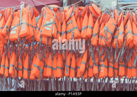 Orange new life jackets for waters sport are hanging on port. Stock Photo