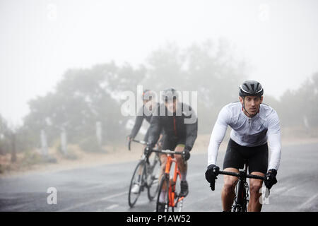 Dedicated male cyclists cycling on rainy road Stock Photo