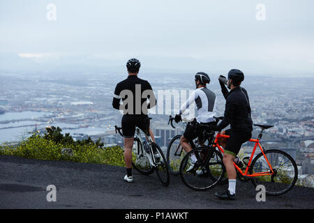 Male cyclist friends taking a break, looking at view from overlook Stock Photo