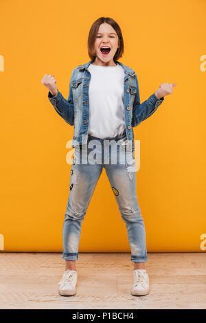 Full length portrait of an excited little schoolgirl screaming over yellow background Stock Photo