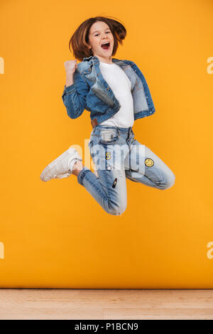 Full length portrait of a happy little schoolgirl jumping over yellow background Stock Photo
