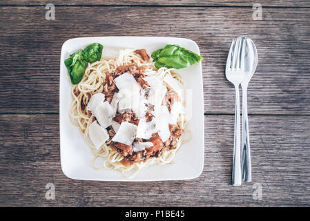 directly above shot of pasta with Bolognese sauce, basil and grated Parmesan cheese on rustic wooden table Stock Photo