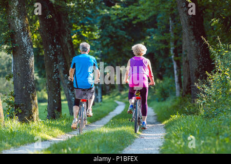 Happy and active senior couple riding bicycles outdoors in the park Stock Photo