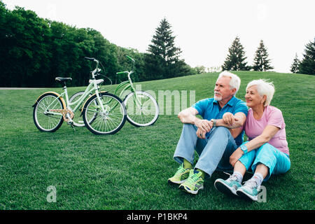 lovely old couple sits on the grass, after riding bicycles Stock Photo