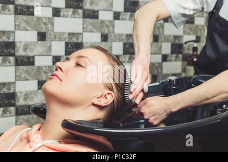 Hair wash procedure in a beauty salon. A hair dresser is washing her clients head in professional sink Stock Photo
