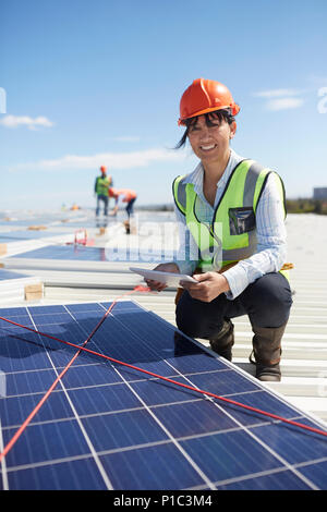 Portrait confident, smiling female engineer with digital tablet examining solar panels at power plant Stock Photo