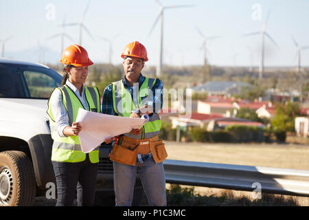 Engineers reviewing blueprints near wind turbine farm Stock Photo