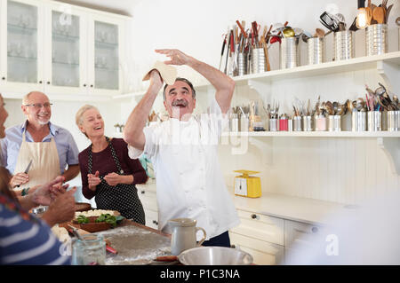 Senior friends watching playful chef tossing pizza dough in cooking class Stock Photo