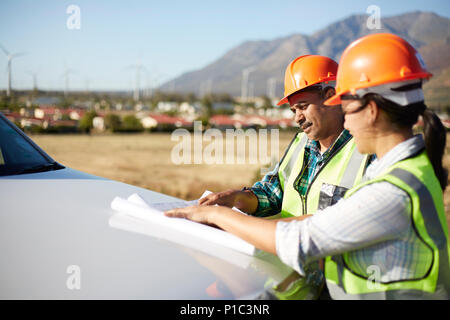 Engineers reviewing blueprints at truck at sunny power plant Stock Photo