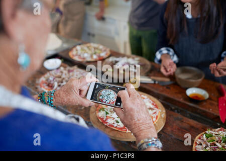 Senior woman with camera phone photographing homemade pizza in cooking class Stock Photo