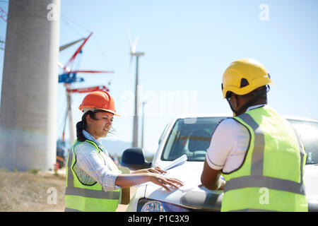 Engineers reviewing blueprints at truck at sunny wind turbine power plant Stock Photo